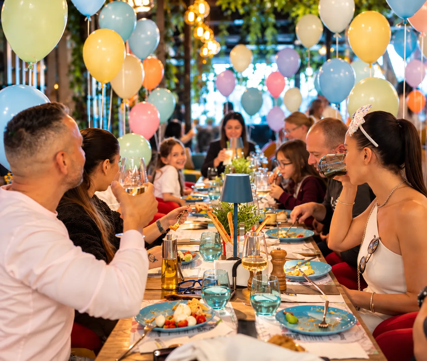 Familii care iau masa împreună la o masă lungă decorată cu baloane la KLANkids